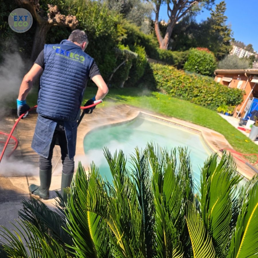 Technicien EXTECO Cannes-Fréjus qui procède au nettoyage vapeur basse pression sur les dalles autour d'une piscine